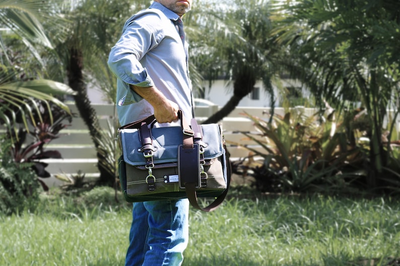 May include: A blue and brown canvas messenger bag with a leather strap and buckle closures. The bag has a front pocket and a large main compartment.