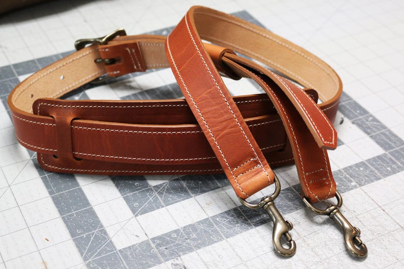 May include: Two brown leather straps with white stitching and silver clasps. The straps are designed for a bag or other accessory.