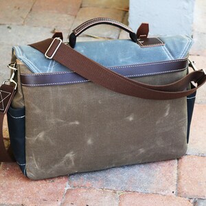 May include: A brown canvas messenger bag with a brown leather handle and strap. The bag has a blue canvas flap with brown leather trim.
