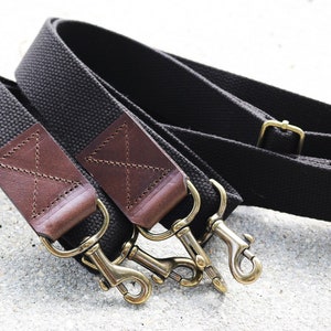May include: Two brown canvas straps with leather accents and gold metal clasps. The straps are folded and the clasps are connected.