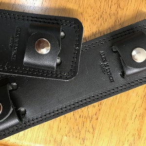 May include: Two black leather guitar straps with metal buckles and the text "Alex M Lynch - Artist" embossed on one strap.