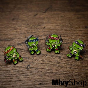 May include: Four enamel pins featuring green cartoon turtles with colored masks. One wears orange, one blue, one red, and one purple. Each turtle holds a different weapon, including nunchucks, katanas, sai, and a bo staff, with black outlines.