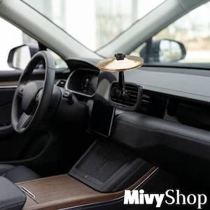 May include: A gold-colored circular magnetic phone mount attached to the black air vent of a car dashboard. The mount features a central black knob and a smooth, metallic gold surface, positioned centrally within the vehicle interior.