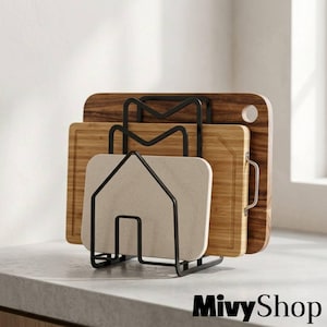 May include: A black metal wire rack holding three rectangular cutting boards of varying sizes and materials. The rack features a house-shaped frame. The boards include a dark wood, a light bamboo wood, and a speckled beige composite material.