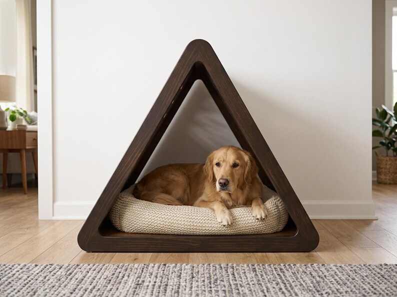 May include: A dark brown wooden pet house with a triangular frame. Inside the structure, a golden-colored dog with long fur is lying down on a thick, cream-colored, textured knit cushion that fills the base of the triangular enclosure.