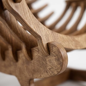May include: A brown wooden rocking chair constructed from layered plywood sheets. The chair features a series of curved, vertical slats that form the seat and backrest, connected by interlocking joints that highlight the natural wood grain texture.