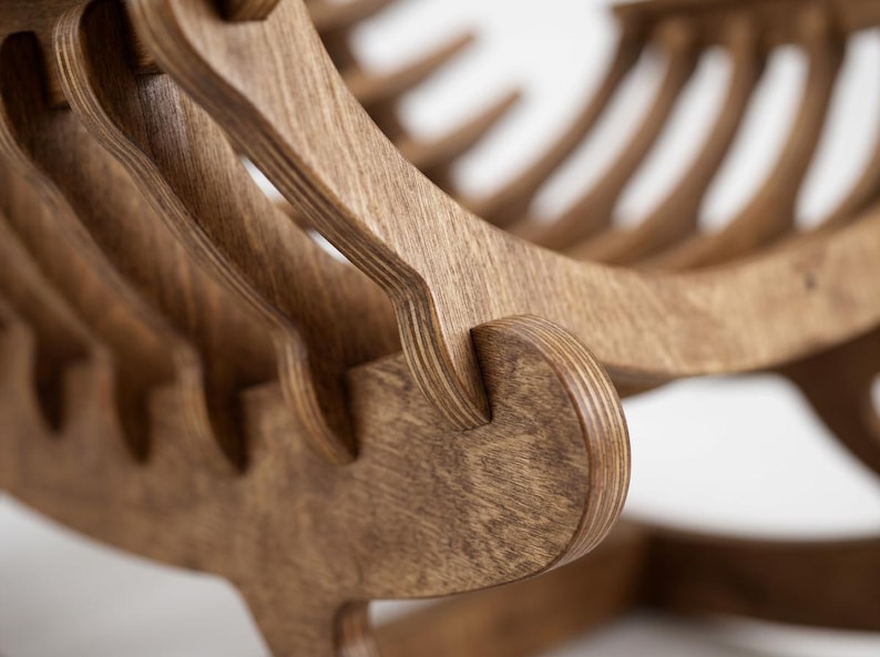 May include: A brown wooden rocking chair constructed from layered plywood sheets. The chair features a series of curved, vertical slats that form the seat and backrest, connected by interlocking joints that highlight the natural wood grain texture.