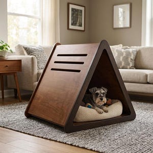 May include: A triangular wooden pet house with a dark brown finish and three horizontal ventilation slats on the side. Inside the structure, a small gray and black dog rests on a round, textured beige cushion placed on the floor.