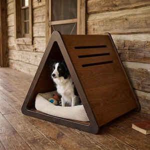 May include: A triangular wooden pet house with a dark brown finish and three horizontal ventilation slats on the side. Inside the structure, a black and white dog sits on a cream-colored textured cushion, accompanied by a small colorful toy.