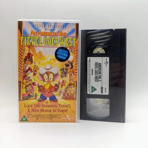 May include: A VHS cassette of the film An American Tail: Fievel Goes West, presented in a clear plastic case with a vibrant illustrated cover depicting Fievel wearing a cowboy hat and the text Look Out Pardners, There's A New Mouse In Town, and a black tape.