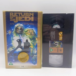 May include: A Return of the Jedi Special Edition VHS tape and its gold-bordered cardboard slipcase. The cover features Star Wars characters, a gold circular sticker, and a green U rating symbol. The black cassette has a matching label and rating.