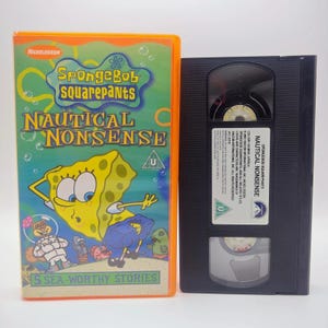 May include: A SpongeBob SquarePants Nautical Nonsense VHS tape in an orange plastic case. The cover features SpongeBob, Sandy Cheeks, and other characters with the text 5 Sea-Worthy Stories. The black VHS cassette has a white label with text.