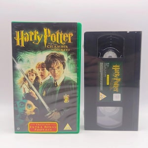 May include: A Harry Potter and the Chamber of Secrets VHS tape and its green plastic case. The cover features Harry Potter, Ron Weasley, Hermione Granger, and Dobby with the movie title in yellow text and a red box stating Includes Extra Bonus Footage.