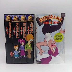 May include: A Futurama Season 4 DVD box set featuring four black spine cases with character illustrations and a clear outer sleeve. The sleeve displays a graphic of Leela hanging upside down and a yellow sticker stating EXCLUSIVE GLOW IN THE DARK PACKAGING.