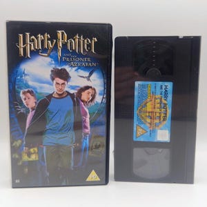 May include: A black plastic VHS cassette tape and its matching cardboard slipcase for the movie Harry Potter and the Prisoner of Azkaban. The cover features the film title, a central character illustration, and a PG rating symbol in the corner.