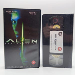 May include: A black VHS case for the film Alien Resurrection featuring Sigourney Weaver and Winona Ryder, alongside the matching black VHS tape with a white label displaying the title, the 20th Century Fox logo, and an 18 age rating symbol.