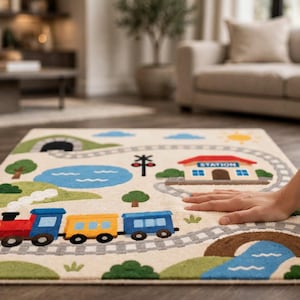 May include: A rectangular area rug featuring a colorful train track design on a cream background. The rug displays a red, yellow, and blue train, a blue pond, green hills, a brown bridge over a blue stream, and a building labeled STATION.
