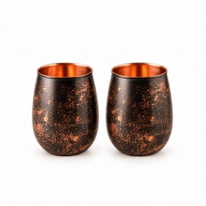 Puede incluir: Dos vasos sin tallo con un acabado exterior oscuro y texturizado con tonos metálicos cobrizos visibles. El interior de cada recipiente muestra una superficie de cobre lisa y pulida, creando un contraste marcado con la capa exterior oscura.