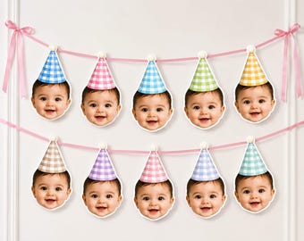 May include: A decorative banner featuring two rows of ten cutouts of a smiling baby face wearing a party hat. Each hat has a different coloured gingham pattern, including blue, pink, green, yellow, brown, purple, and teal, suspended by pink ribbon.