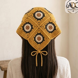 Puede incluir: Un pañuelo de ganchillo con un patrón de cuadrados de la abuela inspirado en girasoles en tonos amarillo mostaza, gris oscuro y beige. La prenda termina en punta en la parte posterior e incluye dos lazos de ganchillo a juego para atar.