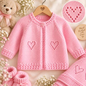 Può includere: Un cardigan lavorato a maglia rosa chiaro con scollo rotondo, chiusura a bottone singolo e motivi a cuore traforati sul davanti. Il capo presenta maniche lunghe con polsini testurizzati e un orlo abbinato. Un'etichetta circolare riporta Hand Knitted with Love.