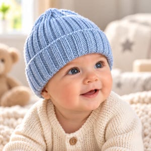 Puede incluir: Un gorro de punto azul claro con textura acanalada y borde doblado. El gorro está confeccionado en hilo y presenta un diseño clásico de corona redondeada. El material muestra un patrón de puntadas verticales consistente en toda la pieza.