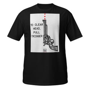 May include: A black short-sleeve t-shirt featuring a white rectangular graphic on the chest. The graphic displays a black and white illustration of a revolver, three red dots above the barrel, and the text TO CLEAR HEAD, PULL TRIGGER.