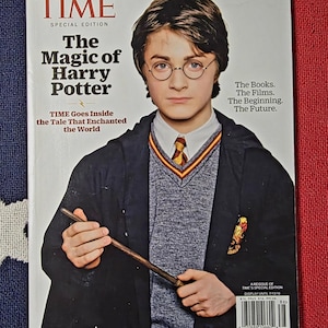 May include: A TIME Special Edition magazine cover titled The Magic of Harry Potter featuring a portrait of Harry Potter wearing round glasses, a white collared shirt, a striped tie, a grey V-neck sweater, and a black robe while holding a wand.