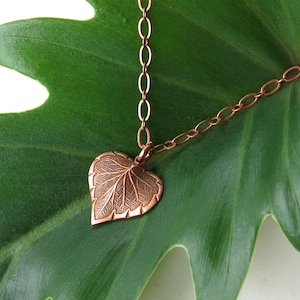 May include: A copper necklace with a detailed leaf pendant. The pendant is shaped like a heart and has a textured surface.