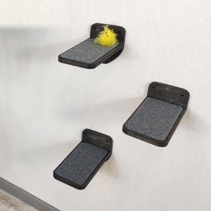 May include: Three wall-mounted shelves made of dark stained wood, each featuring a rectangular gray felt pad on the surface. The top shelf includes a small, fluffy yellow toy. These shelves are designed for vertical installation on a flat surface.