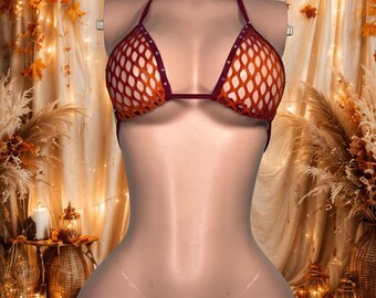 Può includere: Un set bikini a due pezzi composto da un top all'americana e uno slip a perizoma. Entrambi i pezzi sono realizzati in tessuto a rete color rosso scuro e arancione, impreziositi da piccole borchie color argento lungo i bordi. Lo slip presenta laccetti trasparenti.