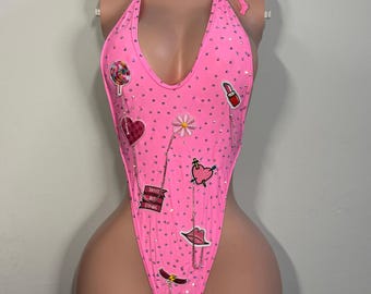 May include: A bright pink halter-style bodysuit covered in small clear rhinestones. The garment features various embroidered patches including a lollipop, a heart, a flower, a lipstick, lips, and a banner with the text "SWEET BUT STING".