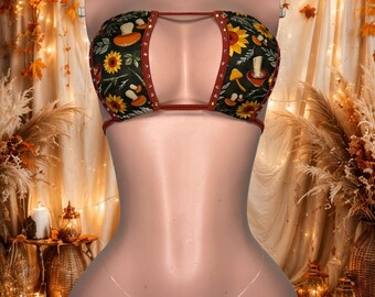 Può includere: Un set bikini a due pezzi in tessuto verde scuro con un motivo ripetuto di girasoli gialli e vari funghi. Il top e lo slip sono rifiniti con tessuto color ruggine e decorati con piccoli strass trasparenti lungo i bordi.