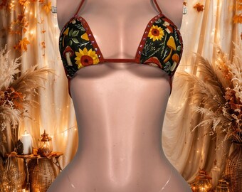 Può includere: Un set bikini a due pezzi con base in tessuto nero e una stampa colorata di girasoli gialli, vari funghi e fogliame verde. I bordi sono rifiniti in tessuto color ruggine con piccoli strass incastonati e spalline trasparenti.