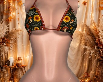 Può includere: Un bikini a due pezzi in tessuto verde scuro con un motivo ripetuto di girasoli gialli, funghi bianchi e fogliame verde. Il top e lo slip sono rifiniti con un bordo color ruggine e decorati con piccoli strass trasparenti e scintillanti.