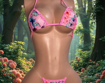 Può includere: Un set bikini a due pezzi con base di colore rosa e una stampa multicolore di farfalle e fiori. Il top è a triangolo con sottili spalline rosa, mentre lo slip è un perizoma con laccetti laterali trasparenti e bordini di colore rosa.