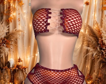 Può includere: Un completo a due pezzi composto da un top a fascia senza spalline e pantaloncini abbinati, entrambi realizzati in tessuto a rete rosso scuro e arancione. Il top presenta un'allacciatura frontale con sottili cordini bianchi e borchie argentate.