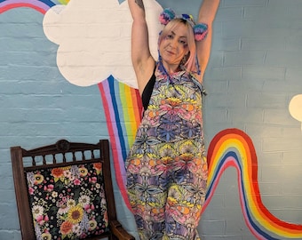 May include: A person wearing a colorful patterned jumpsuit with a rainbow background. The person is wearing a headband with pom-poms.