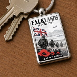 May include: A rectangular metal keyring featuring a graphic of soldiers, a Union Jack flag, and a helicopter. The text reads FALKLANDS 14 JUNE 1982 and LEST WE FORGET, with red poppy flowers at the bottom. Two silver keys are attached to the ring.