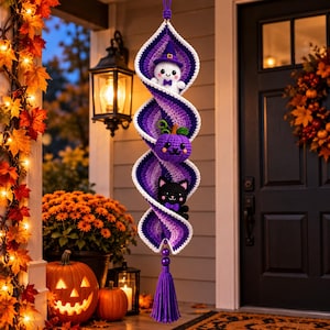 May include: A spiral crochet hanging decoration featuring a white ghost wearing a purple witch hat, a purple pumpkin, and a black cat. The piece is crafted in shades of purple and white yarn, finished with a purple tassel and hanging loop.