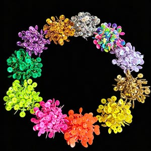 May include: A circular arrangement of numerous small, round push pins in a variety of vibrant colors including gold, silver, purple, green, lime, pink, orange, yellow, and light blue, each featuring a sharp metal point for securing documents.