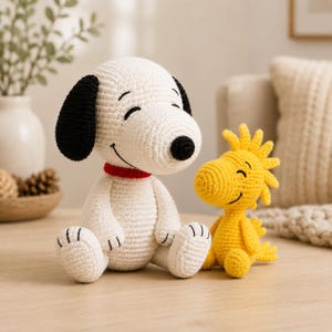 May include: A white and black crocheted dog plush toy with a red collar sitting next to a smaller yellow crocheted bird plush toy. Both figures have embroidered black eyes and smiles, featuring a textured yarn construction throughout.