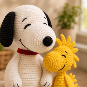 May include: A crochet plush toy set featuring a white dog with black ears, a black nose, and a red collar, standing next to a smaller yellow bird plush toy. Both figures have stitched closed eyes and smiling expressions, crafted with visible yarn texture.