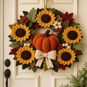 May include: A round wreath featuring crocheted sunflowers with yellow petals and dark brown centers, interspersed with green and red crocheted leaves, small white and red berries, a central orange crocheted pumpkin, and a beige crocheted bow.