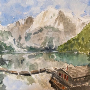May include: Watercolor painting of a lake with mountains in the background. A small wooden cabin sits on the shore of the lake. Several boats are docked at the cabin.