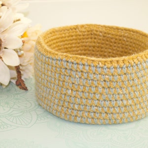 May include: A crocheted basket with a light blue and yellow striped pattern. The basket is made of a natural fiber and has a round shape.