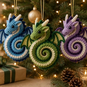 May include: Three crocheted dragon ornaments in blue, green, and purple, each featuring a coiled tail, small wings, and cream-colored horns. These yarn creatures are suspended by gold strings, showcasing detailed stitching and black bead eyes.