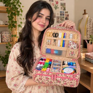 May include: A rectangular floral print sewing organizer case with a top handle and zipper closure. The interior features elastic loops for scissors and pens, a mesh pocket, a pin cushion, and multiple compartments filled with colorful thread spools.