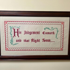 May include: A framed cross-stitch with the text "His Judgement Cometh and that Right Soon..." in red lettering on a white background. The cross-stitch is surrounded by a red and green border.