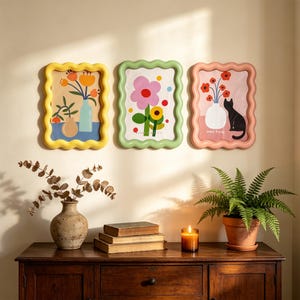 Peut inclure: Trois cadres muraux rectangulaires aux bords ondulés et festonnés, de couleur jaune, vert clair et rose. Chaque cadre contient une illustration colorée : un vase avec des fleurs orange, une grande fleur rose et un chat noir près d'un vase de fleurs rouges.